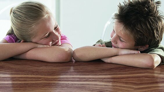 Zwei Kinder welche auf ihren verschränkten Armen liegen und sich anlächeln