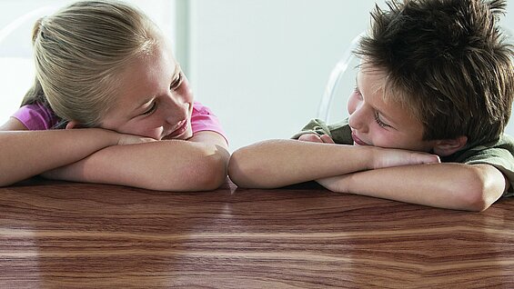 Zwei Kinder welche auf ihren verschränkten Armen liegen und sich anlächeln